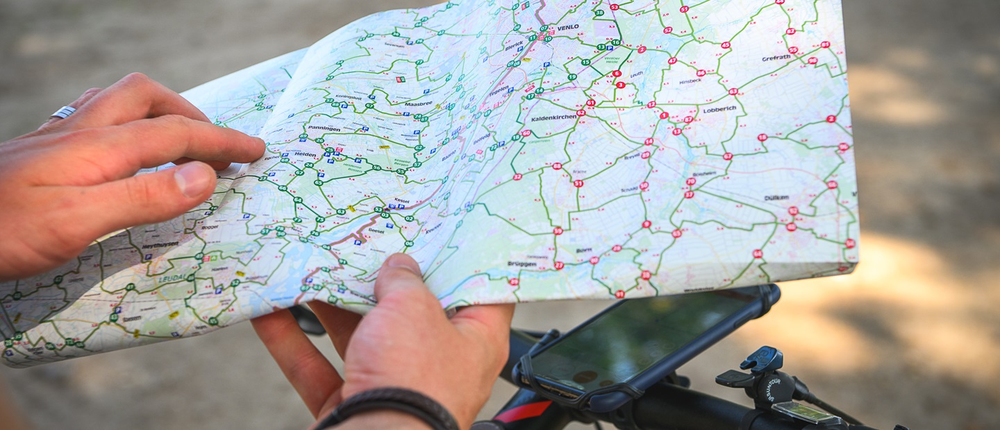 Fietser bekijkt een knooppuntenkaart van Limburg boven een smartphone op het stuur.