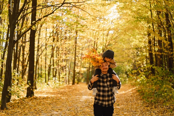 Sohn sitzt bei einem Waldspaziergang in den Herbstferien auf Papas Hals