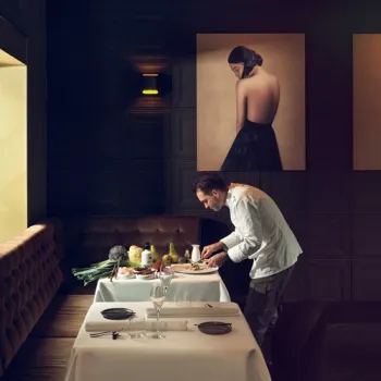 Chef maakt een gerecht op aan een gedekte tafel in een sfeervol restaurant.