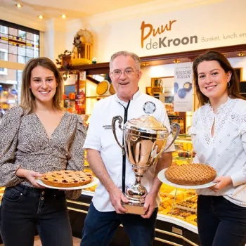 Frank Smeets staat met een grote beker tussen zijn twee dochters, die Limburgse vlaaien vasthouden in Banketbakkerij - Lunchroom In de Kroon.